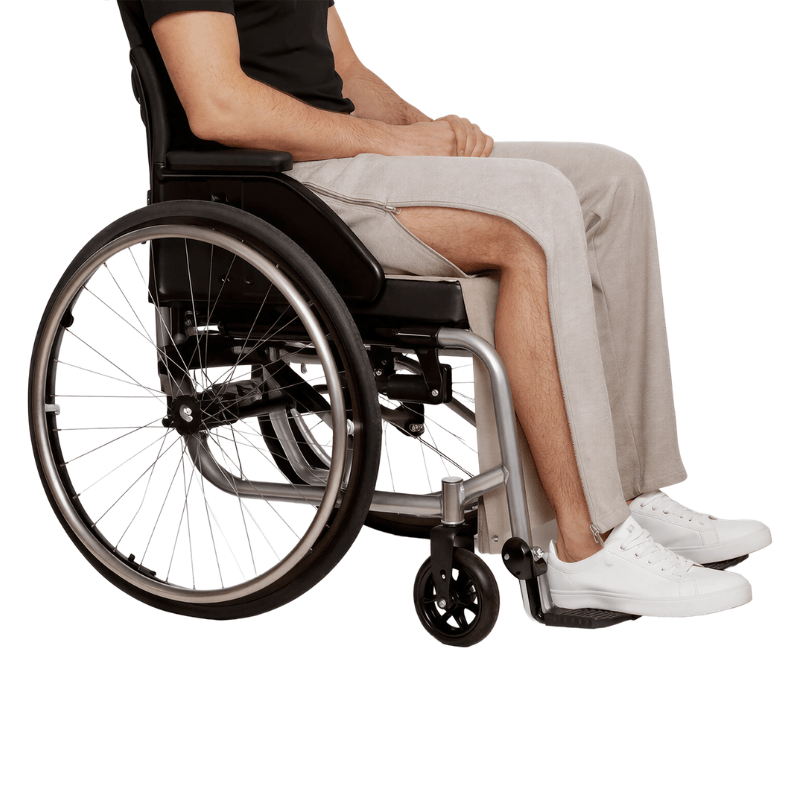 Een persoon in een rolstoel draagt een grijze joggingbroek met open zijrits die het been toont