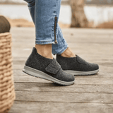 Vrouw draagt antracietgrijze New Feet pantoffels op een houten vloer, zijaanzicht van de voeten