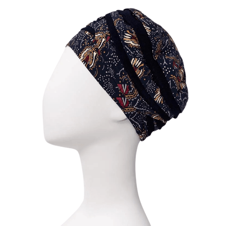 Shanti tulband in Amber Garden print van de zijkant op witte paspop, met donkerblauwe basis en veren- en stengelmotief