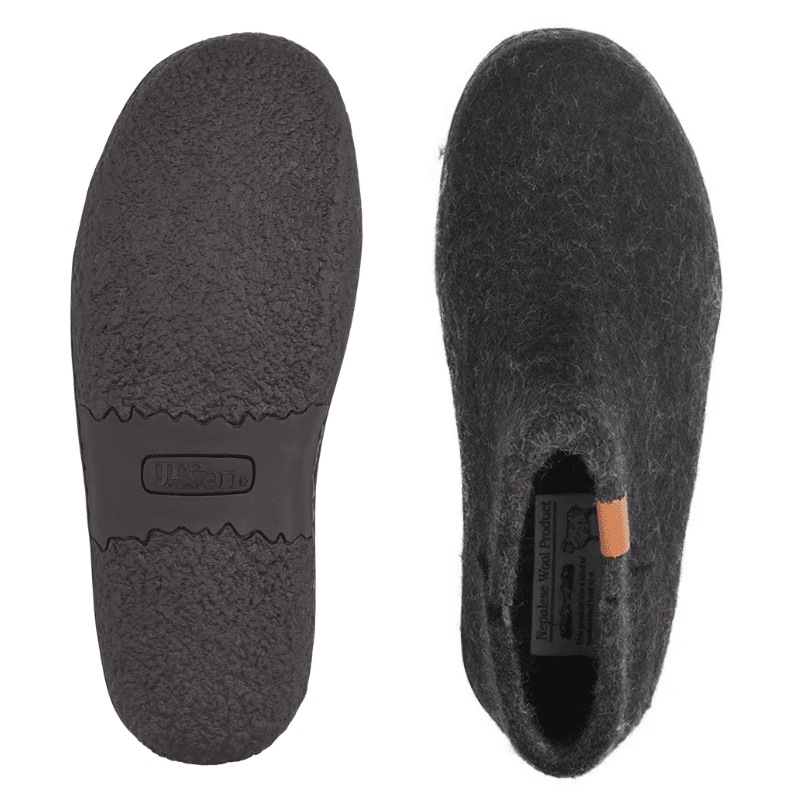Twee zwarte Green Comfort pantoffels van wolvilt, de ene toont de antislip rubberen zool, de andere de bovenkant